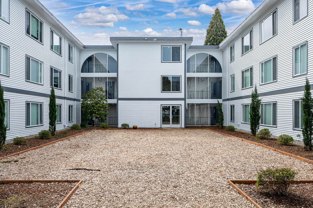 the courtyard of a white apartment building with a gravel area and trees